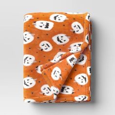 an orange blanket with black and white ghost faces on it, folded in front of a gray background