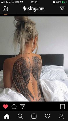 a woman sitting on top of a bed with an angel tattoo on her upper back