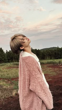 a woman standing in a field with her eyes closed wearing a pink sweater and jeans