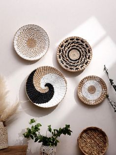 four woven baskets hanging on the wall next to a potted plant and wicker basket