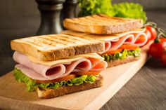 a sandwich with ham, lettuce and tomatoes on a cutting board