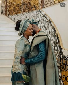 a man and woman standing next to each other in front of a stair case holding hands