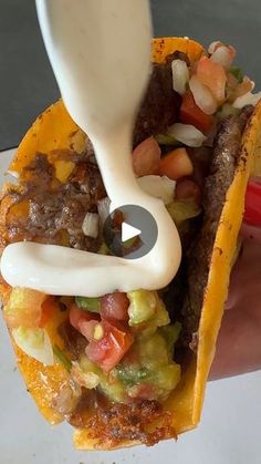 a hand holding a taco filled with meat and veggies on top of it