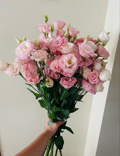 a person holding a bunch of pink flowers in their hand with white walls behind them