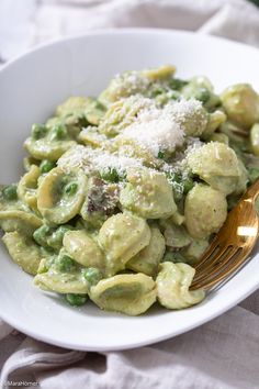 a white bowl filled with pasta covered in pesto sauce and parmesan cheese