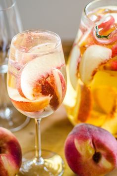 two glasses filled with liquid and sliced peaches on a wooden table next to apples