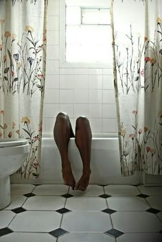 a person is sitting on the edge of a bathtub in front of a window