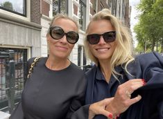 two women standing next to each other in front of a building wearing sunglasses and jackets