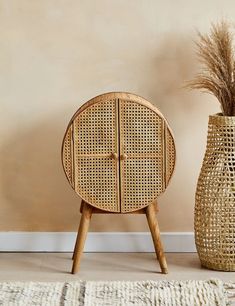 a round wooden table next to a vase with dried grass in it and a rug on the floor