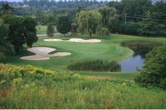 a golf course surrounded by trees and water in the foreground, with a pond at the far end