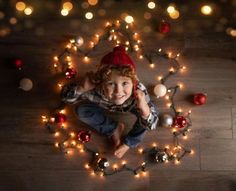 a young boy is laying on the floor surrounded by christmas ornaments and lights, looking up at the camera