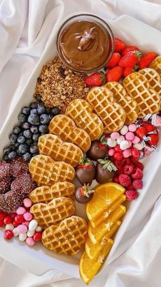 a white plate topped with waffles and fruit next to a bowl of chocolate