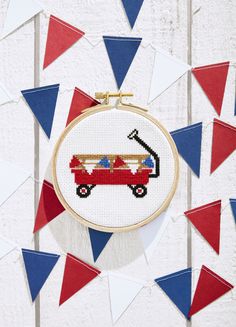 a cross stitch pattern with a red wagon on it and blue, white, and red flags in the background