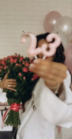 a woman holding flowers and balloons in front of her face with the number 20 on it