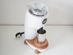 a white coffee maker sitting on top of a wooden stand next to a cup holder