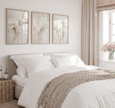 a bedroom with white bedding and paintings on the wall