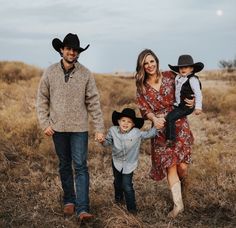 a man, woman and two children walking in a field holding hands with each other