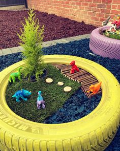 a yellow tire with toy dinosaurs in it and some fake plants growing out of it