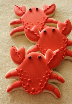 three cookies decorated with red and white icing on top of each other, one is shaped like a crab