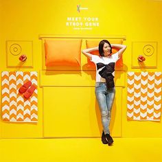 a woman leaning against a yellow wall with orange and white pillows on it's sides