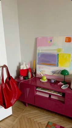 a red purse sitting on top of a wooden table next to a wall mounted painting