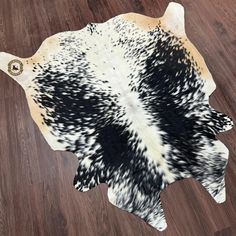 a cowhide rug with black and white spots on it's back end, laying on a wooden floor