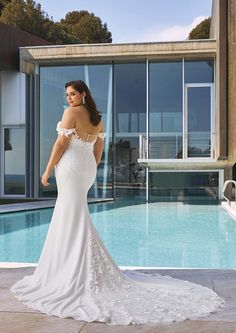 a woman standing in front of a pool wearing a wedding dress with off the shoulder sleeves