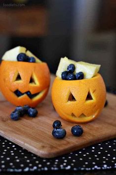 two oranges with faces carved into them and blueberries on the bottom one is cut in half to look like jack - o'lanterns