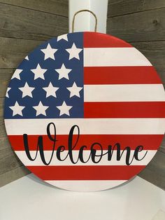 a welcome sign with an american flag painted on the front and back, hanging from a hook