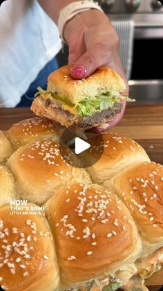 a person holding a sandwich in front of some buns on a cutting board with sesame seeds