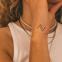 a woman with a small tattoo on her left arm and wrist is holding her hand up to her face