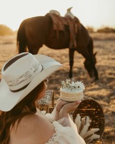 a woman in a white dress and cowboy hat holding a cake with flowers on it