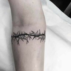 a black and white photo of a barbed wire tattoo on the left leg, with an arrow in the middle