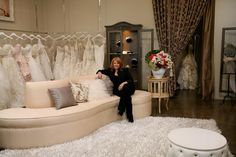 a woman sitting on top of a couch in a room filled with wedding gowns