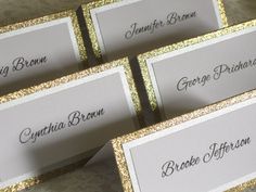 there are four place cards with gold glitter border on the top one is white and has black lettering