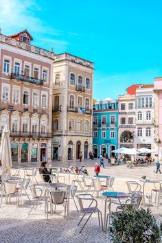 people are sitting at tables and chairs in the middle of an open square with many buildings