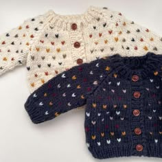 three knitted sweaters sitting next to each other on a white surface with buttons