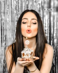 a woman blowing out the candles on a cake that is being held by her hands