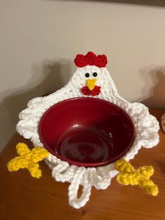 a crocheted chicken sitting on top of a table next to a red bowl