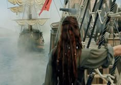 a man with dreadlocks standing on the deck of a ship looking at another boat