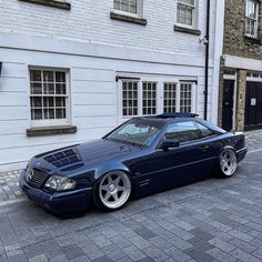 a blue car parked in front of a white brick building on a cobblestone street