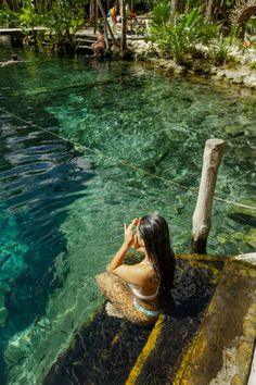 a woman sitting on the edge of a body of water next to a wooden dock