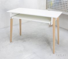 a white desk with wooden legs in an empty room next to a metal grate