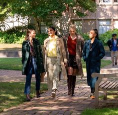 four young women walking down a brick walkway in front of a building with trees and grass