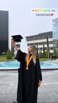 a woman wearing a graduation gown and holding up her cap in front of a fountain