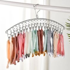 several scarves hanging from a metal rack in front of a white curtain and window