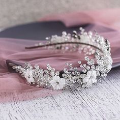 a tiara with flowers and pearls on it sitting on a pink cloth next to a book