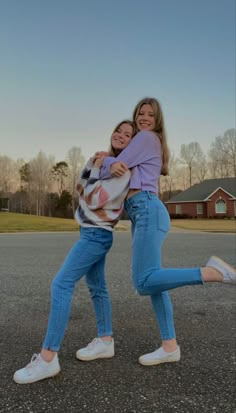 two girls are hugging in the middle of an empty parking lot with their arms around each other