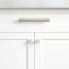 a white cabinet door with two knobs and a metal handle on the bottom drawer