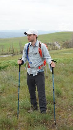 a man standing on top of a lush green field holding ski poles and wearing a hat